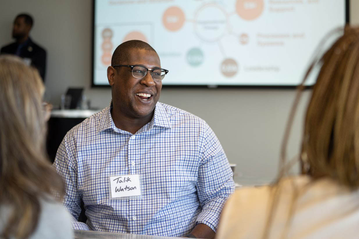 College with name tag. Smiling and wearing glasses.